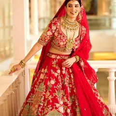 A closer view of the bridal look, focusing on the detailed embroidery of the lehenga and the exquisite gold jewellery. The model's joyful expression captures the happy spirit of a wedding celebration.