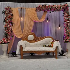 A modern and chic engagement stage design. The combination of peach draping, an asymmetrical floral arch, and industrial-style hanging lights creates a sophisticated and stylish backdrop.