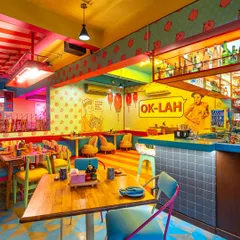 This view of The Fatty Bao shows the interplay between different sections of the restaurant. The "OK-LAH" wall art and varied seating arrangements are framed to showcase the dynamic and multi-layered design of the space.