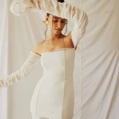 An all-white look from a creative fashion shoot. The styling, featuring a structured top with dramatic, ruched off-shoulder sleeves, creates an ethereal and sculptural silhouette against the simple white backdrop.