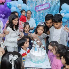 The birthday girl, dressed as a princess, surrounded by her friends and family for the cake-cutting. The Frozen-themed cake completes the magical celebration.