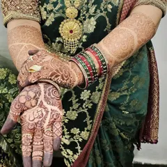 A beautiful view of the developing henna stain, paired with a stunning green saree and traditional jewelry. The deep color on the palm highlights the intricate details and the groom's name.