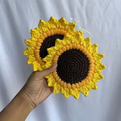 A hand holding two of our detailed crochet sunflower coasters. This view shows the texture and two-tone color work that makes them look so vibrant.
