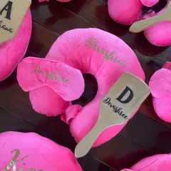 A close-up of the personalized travel favor set, showing the custom name detail on the pillow, eye mask, and hairbrush.
