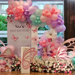 A vibrant fairy and butterfly garden theme for Sia's first birthday. This setup is packed with details, including mushroom props, large butterfly wing cutouts, and a lush organic balloon arch in pink, purple, and mint green.