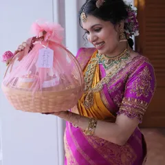 A happy client holding a fully wrapped 'Valakappu' return gift basket, adorned with pink tulle and a custom tag. It’s a beautiful way to thank guests for their blessings.