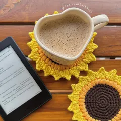Our crochet sunflower coaster in action, pictured with a coffee mug and a Kindle. It's the perfect companion for a relaxing morning, protecting your surfaces with a touch of handmade charm.