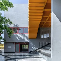 L'Atelier at Greenwood High School uses a simple palette of grey plaster punctuated by bold primary colors. The yellow underside of the staircase creates a vibrant, playful intervention, reflecting the creative energy of the art and music school within.