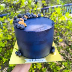 Blueberry bliss. A tall, elegant cake with a deep blue, textured buttercream finish, topped with a crescent of fresh, juicy blueberries.