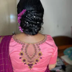 A chic and elegant messy bun, decorated with purple flowers to match the client's blouse. This is a great option for a reception or party.