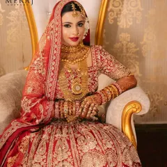 A portrait of bridal regality. The bride is seated, showcasing the full splendor of her eternal red lehenga, rich with detailed embroidery and traditional craftsmanship.