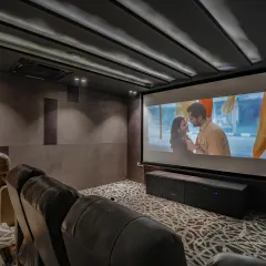 The home theater in our Vikaspuri project, shown with the large screen in action. The setup includes surround sound speakers and a dark, moody color scheme for an immersive viewing experience.