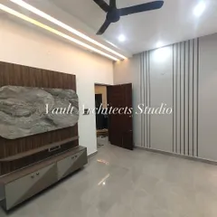 A wide view of a minimalist bedroom. The space is defined by a sleek TV unit with a marble and wood-finish backdrop, clean wall paneling, and a modern ceiling design with integrated lighting.