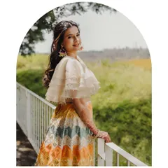 A portrait of a happy client in her custom chevron-patterned lehenga. The organza cape-style blouse with pearl detailing adds a modern and playful touch to this pre-wedding outfit.