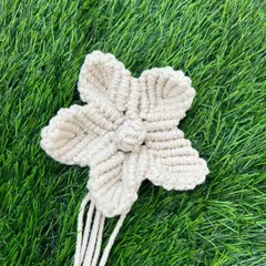 A single, beautifully knotted macrame flower against a green background. These flowers can be used as decorative accents on their own or as part of a larger piece.