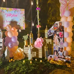 Here is a wider view of an outdoor first birthday party we organized. The setup includes a personalized welcome sign, balloon arrangements, and a beautiful decor corner with a photo collage and lanterns, all lit by charming string lights.