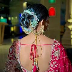 An elegant and clean bridal bun, beautifully decorated with a semi-circle of fresh baby's breath and other delicate flowers. This updo is perfect for securing a dupatta and provides a classic, polished look for the wedding pheras.