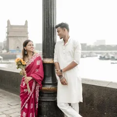 A sweet moment during a pre-wedding shoot at the Gateway of India, where the bride in a red saree holds a bouquet of sunflowers while looking lovingly at her partner.