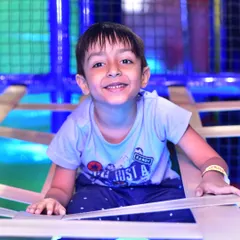 A happy boy smiles from the top of a climbing structure, proud of his accomplishment.