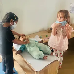 Two young "doctors" are carefully tending to their patient, a baby doll. Role-playing scenarios like this allows children to process their own experiences, like visiting a doctor, in a safe and controlled way.