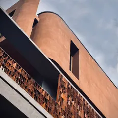 A detail of the façade reveals the rhythmic interplay between the warm, textured terracotta screen and the monolithic, curved structure. This juxtaposition of materials and a focus on refined detailing are central to our architectural language.