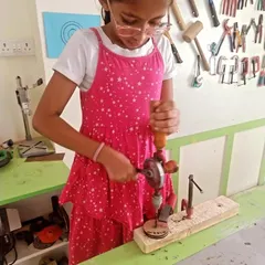This young maker is learning how to use a hand drill with a clamp to hold her workpiece steady. It's a fundamental skill for any woodworker.