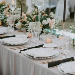 A beautifully set dining table with silver-beaded charger plates, fine cutlery, and a lush floral centerpiece. We work to ensure the tablescape perfectly complements your event's theme and our culinary offerings.