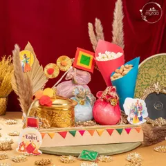 This vibrant Lohri hamper is full of festive cheer. It includes cones of popcorn and peanuts, potlis of sweets, a golden jar, and decorative elements inspired by the harvest festival.