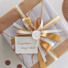 A beautifully wrapped anniversary gift, featuring gold and white ribbons, a wax seal, and a handwritten congratulations card for the couple.
