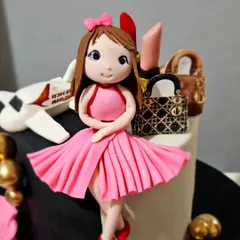 A detailed close-up of the custom figurine for a "favorite things" cake. You can see the texture of her pleated pink dress and the tiny bow in her hair, all sculpted from sugarpaste.