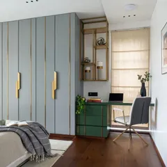 This master bedroom at Park West features a custom wardrobe with a serene blue-grey finish and elegant brass inlay details. Adjacent to it, a compact study nook with a vibrant green desk provides a functional workspace without compromising the room's restful feel.