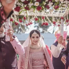 The bride's grand entrance under a beautiful 'phoolon ki chadar'. Her direct gaze at the camera captures her confidence and anticipation in this iconic wedding moment.
