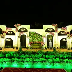 A wide view of the elegant reception stage. The green uplighting on the foliage base adds a pop of color and drama to the otherwise soft and classic white and pink decor.