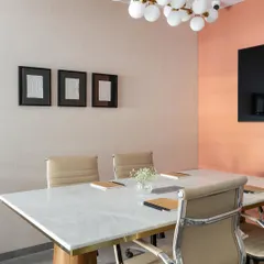 The conference room combines a marble-topped table with comfortable leather chairs and a modern bubble chandelier. The peach-colored accent wall adds a touch of warmth and personality to the space.