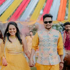 A happy couple walks hand-in-hand under the colourful drapes of their Haldi ceremony. The decor is designed to be bright and cheerful, reflecting the celebratory mood of the event.