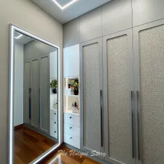 This custom wardrobe features beautiful rattan shutter panels with a grey Duco finish. The design includes a full-length mirror with integrated backlighting, combining natural texture with modern functionality for a stylish storage solution.