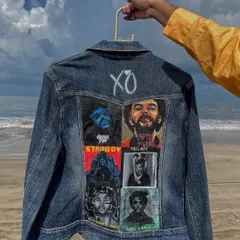 Holding up the finished Weeknd jacket, this shot showcases the entire piece, from the hand-painted 'XO' at the top to the detailed portraits below.