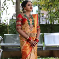This is a classic South Indian muhurtham look. The bride is wearing a beautiful golden-beige Kanchipuram silk saree with a contrasting red border, paired with a heavily embroidered blouse and temple jewelry.