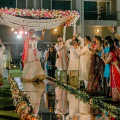 A beautiful bridal entry under a 'phoolon ki chadar' held by her brothers, walking down a mirrored aisle. A perfect blend of tradition and modern elegance.