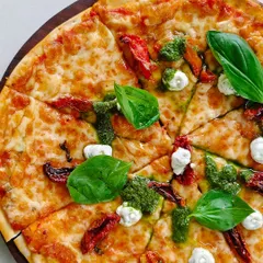 A delicious pizza topped with sun-dried tomatoes, fresh basil, pesto, and creamy goat cheese.