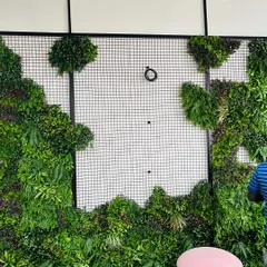 The installation process of a vertical garden. The artificial plant panels are attached to a wire mesh frame on the wall.