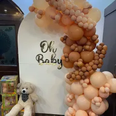 A modern and chic 'Oh Baby' shower decoration. We used a popular neutral color palette with a cascading balloon arch in shades of nude and brown against a clean white arched backdrop, perfect for a sophisticated Godh Bharai ceremony.