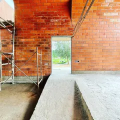 A view through a doorway in the 'Vault & Wall' house, where the rich red of the hollow clay bricks is the primary finish. The ramp provides accessible circulation through the space.