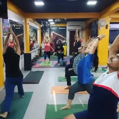 A class holding Veerbhadrasana I (Warrior Pose I). This powerful asana builds strength in the legs, opens the hips and chest, and develops stamina and balance, making it perfect for those who sit for long hours.