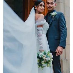 A classic wedding portrait with a touch of drama. The bride's veil flowing in the wind adds a beautiful, dynamic element to this elegant shot outside the church.