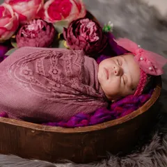 A precious newborn girl wrapped in a lace-detailed swaddle, nestled in a wooden bowl surrounded by flowers. I use soft textures and colors to create a beautiful, artistic portrait.