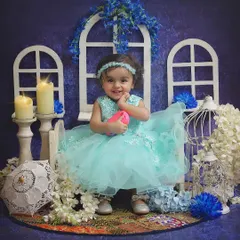 A vision in blue! This sweet little girl is all smiles in our dreamy blue-themed studio setup, complete with white window props, candles, and flowers.