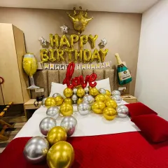 A fun and celebratory birthday decoration with a royal touch. This setup includes gold and silver chrome balloons, 'Happy Birthday' foil letters, and playful additions like a crown, champagne bottle, and wine glass foil balloons.