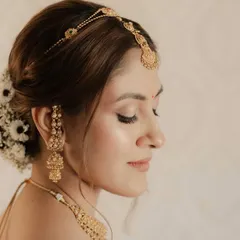 The side profile highlights the intricate bridal bun with fresh flowers and the soft, glowing finish of the skin. Every detail is intentional.