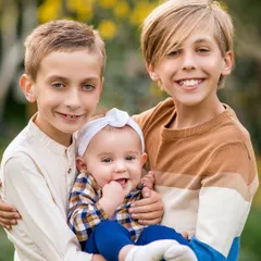 The three siblings together! The two older brothers proudly hold their baby sister, creating a portrait that is overflowing with love and family connection.